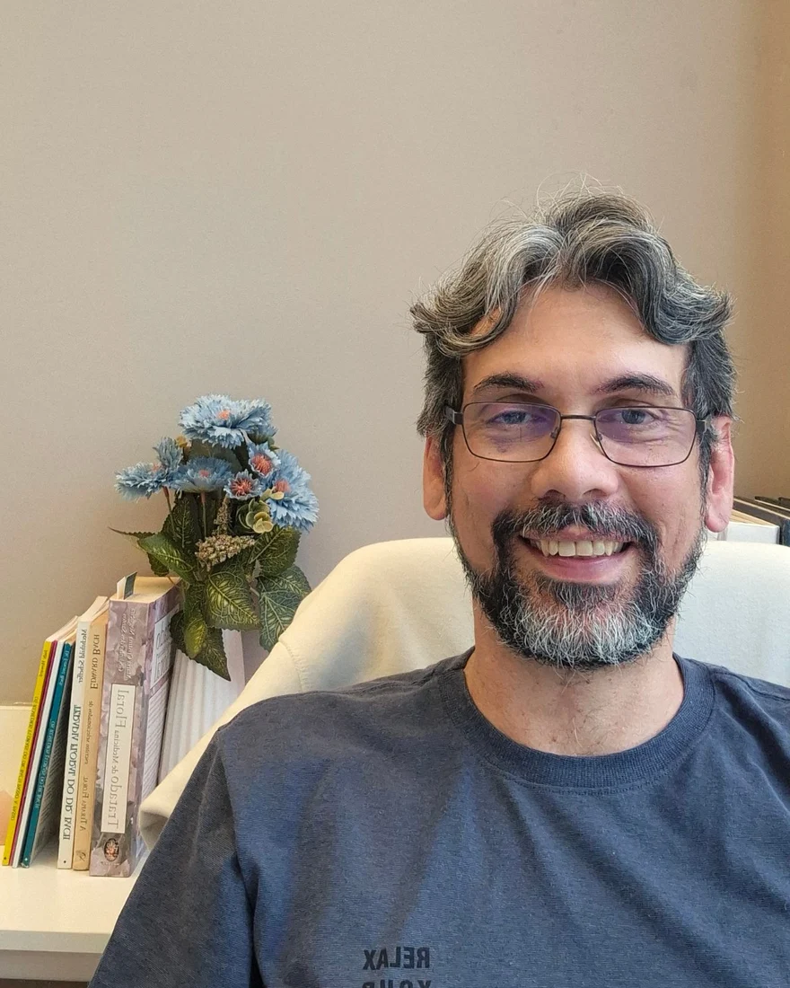 Fábio Leite sorrindo em seu consultório, ao lado de livros sobre os florais de Bach